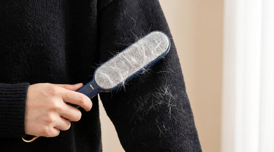 Hand using a lint brush to remove cat hair from a black sweater